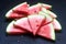 Triangular watermelon slices with seeds on a black concrete background