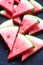 Triangular watermelon slices with seeds on a black concrete background