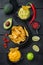 Triangular yellow corn tortilla chip with sauce, on black wooden background, top view or flat lay