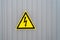Triangular yellow sign of dangerous electrical voltage on the gray wall. Raindrop