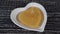 A trickle of bee honey flows in a white heart-shaped plate on a dark old wooden table