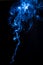 Trickle of vape smoke isolated on black background. Swirls of smoke with blue light, vertical photography for design