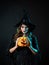 tricky beautiful witch in a pointed hat Holding a pumpkin with a laughing face,