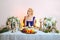 Tricky lady with colorful makeup sitting behind table and eating felt shoe