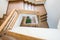 A tricky shape curved wooden staircase or stairway from the top looking down with a green plant in the bottom ground level