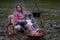 Tricolor Australian Shepherd sits next to a young woman by the campfire. In winter, snow on the grass. The fire is burning under