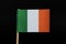 A tricolour flag of Ireland on toothpick on black background. A vertical tricolour of green, white and orange