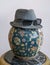 Trilby hat wearing sunglasses over antique decorated Chinese ceramic vase