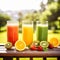 Trio of fresh healthy fruit juice blends in tall glasses on a summer picnic table outdoors with orange