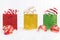 Trio of glittery gift bags in a row on a white background and fur with red and gold Christmas ornaments