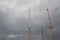 Trio of ship masts, rigging but no sails, against threatening skies with storm clouds