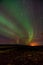 Triple banded northern lights in a smooth bend across the rocky horizon. The last glow of sunlight shimmers on the rocky horizon