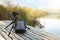 Tripod with modern camera and backpack on wooden pier near water. Professional photography