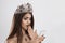 Trolling in social media, shocking bad news. A shocked beauty queen woman with crown looks at the phone she holds in her hand,