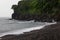 Tropical beach on storm - cape with black rocks, lush green forest and   grey waves of sea with foam in rain.  Trip in rain season