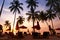 Tropical beach at sunset, tourist hotel resort with silhouettes of palm trees and deckchairs