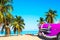 The tropical beach of Varadero in Cuba with american classic pink car, sailboats and palm trees on a summer day with turquoise