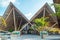 Tropical beautiful landscape view with palm trees, chairs, wooden roofs under blue sky during sunny day