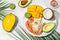 tropical bowl with avocado, prawns, rice, mango, kiwi and coconut, tropical food on the sea beach on light background with