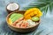 tropical bowl with avocado, prawns, rice, mango, kiwi and coconut, tropical food on the sea beach on light background with