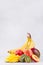Tropical bright fruits - mango, banana, kiwi, pear, peach, nectarine on soft white wood board with copy space, vertical.