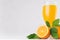 Tropical citrus yellow juice in elegance wineglass closeup with ripe oranges and green leaves on soft white wood background.
