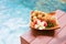 Tropical fruits and plmeria in soft focus on wooden tray near swimming pool