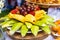 Tropical fruits: sliced guava, jackfruits, grapes, strawberrys laying on the dish served on the decorated table staying outdoor
