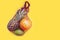 Tropical fruits in a string string bag. pineapple, mango, pomelo. Yellow background. Place for text