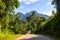 Tropical landscape with greenery and mountains in sunny day. Tropical nature with straight road and forest roadside