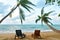 Tropical landscape with two sun loungers under palm tree leaves and sea view