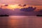 Tropical orange evening sunset and pier. Colorful sky in the dusk. Calm sea and cottage silhouettes above the water.