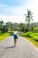 Tropical portrait of young happy woman with straw hat on a road with coconut palms and tropical trees. Bali island.