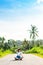 Tropical portrait of young happy woman with straw hat on a road with coconut palms and tropical trees. Bali island.