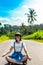 Tropical portrait of young happy woman with straw hat on a road with coconut palms and tropical trees. Bali island.