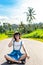 Tropical portrait of young happy woman with straw hat on a road with coconut palms and tropical trees. Bali island.