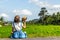 Tropical portrait of young happy woman with straw hat on a road with coconut palms and tropical trees. Bali island.