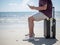 Tropical sea, Young man sitting on Travel suitcase and using smart phone at the beach. Summer holiday traveling concept design