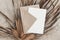Tropical stationery still life. Closeup of blank card mock-up and craft envelope. Dry palm leaf on grunge beige concrete