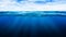 Tropical underwater dark blue deep ocean wide nature background with rays of sunlight and blue sky in background.