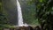 Tropical waterfall in lush green jungle. Falling water hitting water surface. Green leaves moved by the wind breeze