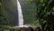 Tropical waterfall in lush green jungle. Falling water hitting water surface. Green leaves moved by the wind breeze