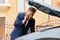 Troubled young businessman talking on phone near broken car