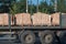 Truck carries wooden pallets with stacked red bricks on open platform of long trailer against the background of roadside trees