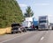 Truck driver changes punctured wheel of the big rig semi truck on the shoulder side of highway next to trucks and cars passing by