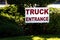 Truck entrance sign on green grass with trees and bushes