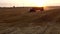 Truck loaded with haystacks drives through wheat field after harvest at sunset