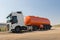 A truck with an orange tank goes on a knurled unpaved road