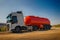 A truck with an orange tank goes on a knurled unpaved road