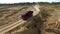 Truck rides on dusty road. Scene. Top view of dump truck driving on clay dirt road of open pit leaving trail of dust